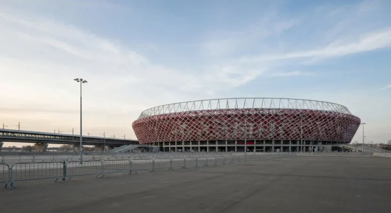 Nowoczesny narodowy stadion w Warszawie z biało-czerwoną ażurową fasadą nad pustym placem po praskiej stronie Wisły